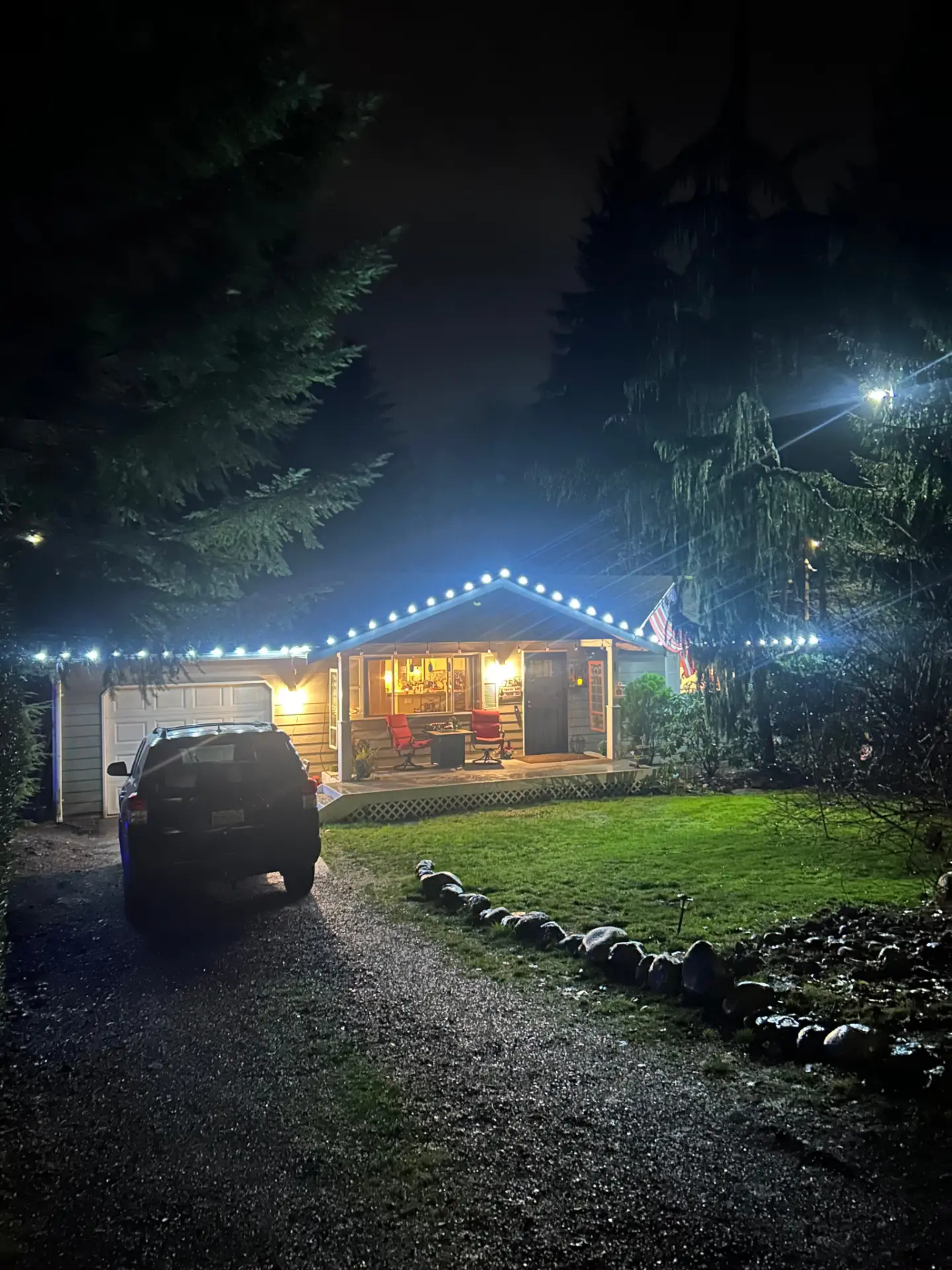 Night view of a Western Washington home with warm white roofline Christmas lights and a lit indoor tree